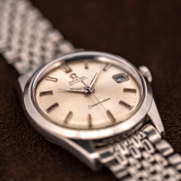 Omega Seamaster 166.010 at an angle, dauphine hands over a silver sunburst dial with steel bracelet