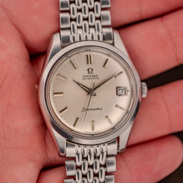 Omega Seamaster 166.010 held in hand, silver dial with date at three and steel beads-of-rice bracelet