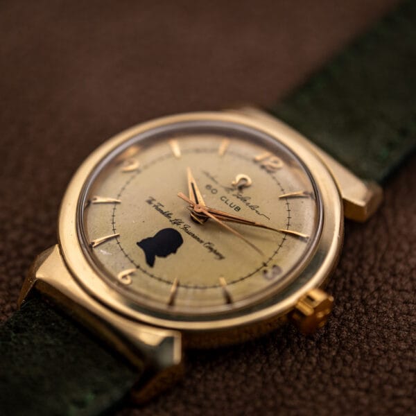 Omega hooded lugs case in gold cap, three-quarter view showing scarab-form lugs and aged presentation dial