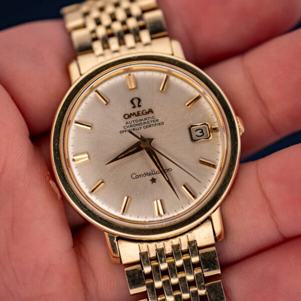 Vintage Omega Constellation 168.004 held in hand, silver chronometer dial with date window and gold bracelet