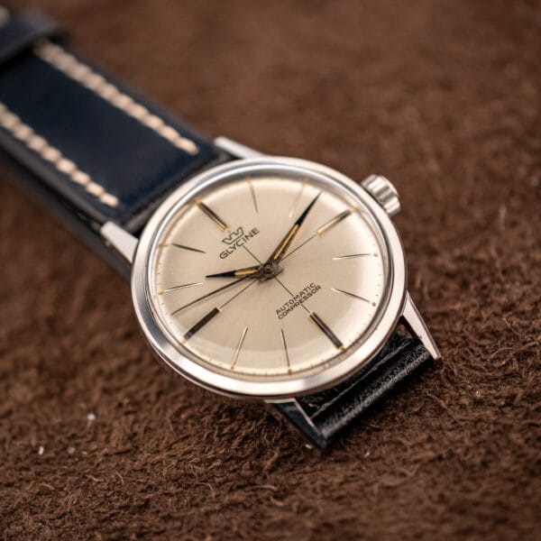 Glycine Compressor ref. 645 flat lay on black leather strap showing the full silver sunburst dial