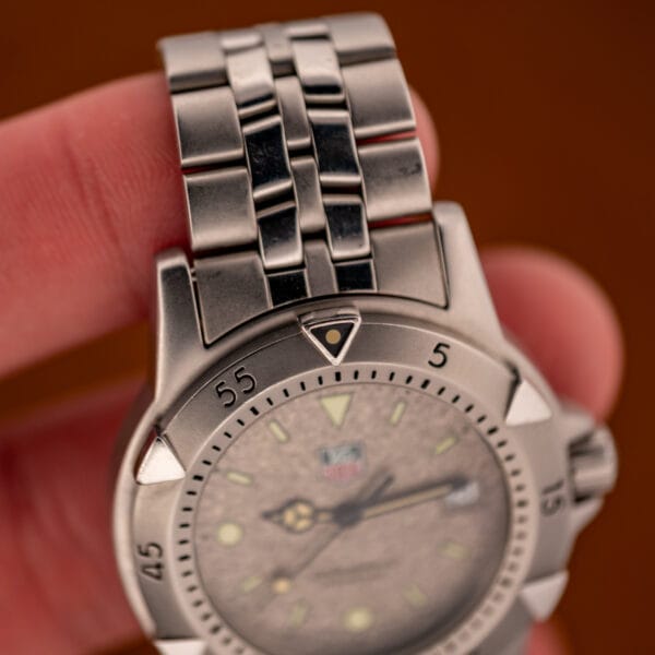 TAG Heuer 1500 Series bezel and bracelet detail with lume pip at twelve, held between fingers