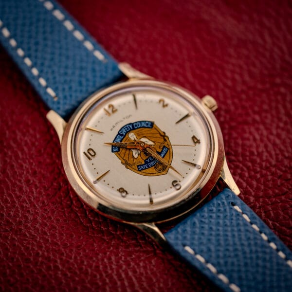 Hamilton Thin-O-Matic Safe Driver Award watch shot top-down on red leather, blue strap and gold filled case