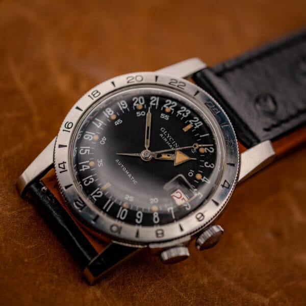 Glycine Airman GMT black 24-hour dial with red date at lower right, angled on tan leather