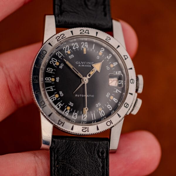 Glycine Airman GMT in hand, black 24-hour dial with red date and broad arrow hour hand