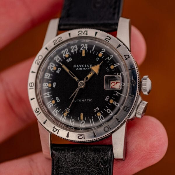 Vintage Glycine Airman automatic held in fingers, 24-hour dial, twin crowns and ostrich strap