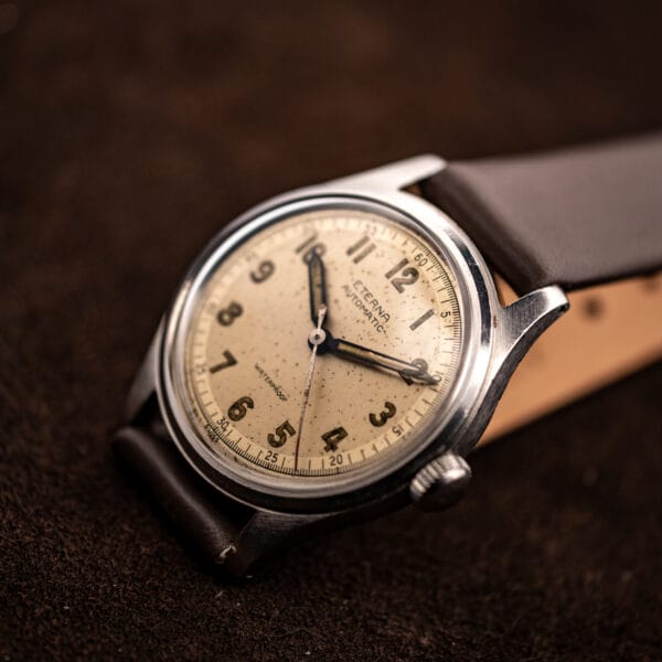 Low-angle view of vintage Eterna Cal. 835 showing domed crystal, cream military dial and steel case