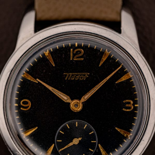 Tissot 6769 black gilt dial close-up showing the cursive Tissot signature, gold dauphine hands and faceted dagger markers