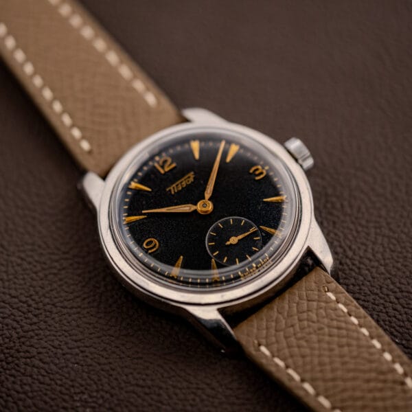 Vintage Tissot 6769 reclined on grey leather strap showing galaxy patina across the black gilt dial