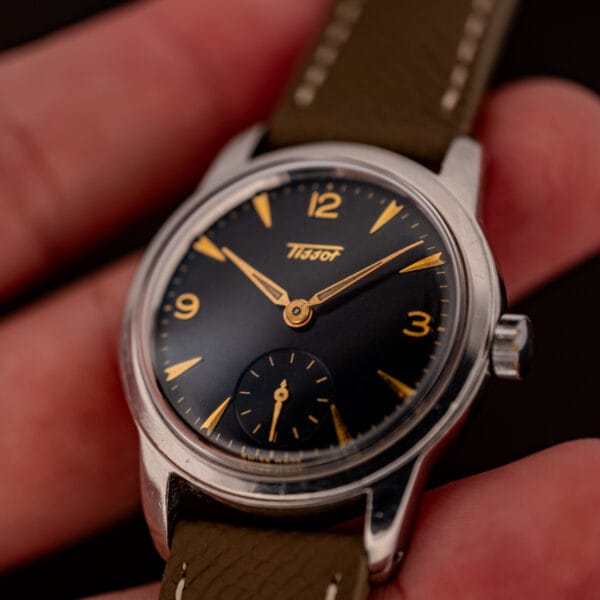 Tissot 6769 wrist-side view in hand, warm black gilt dial with gold faceted markers on grey strap