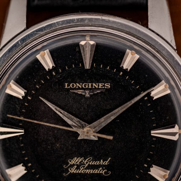 Longines winged hourglass logo and applied dart markers on aged black All Guard dial, macro