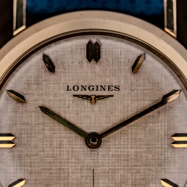 Longines 1116 linen dial macro showing the cross-hatch finish and winged hourglass logo beneath the LONGINES signature