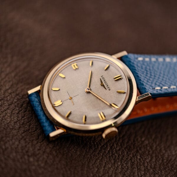 Vintage Longines linen dial dress watch angled view with faceted lugs and blue leather strap