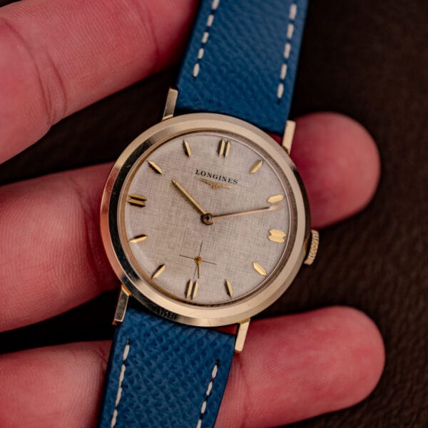 Vintage Longines 1116 held in hand showing linen dial and gold dauphine hands in a gold filled case