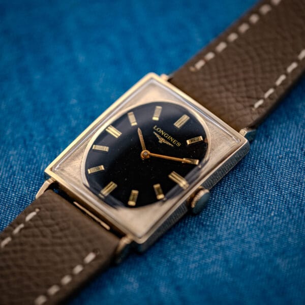 Longines Tank 3007-528 three-quarter view showing engine-textured gold-filled case face and oval black dial