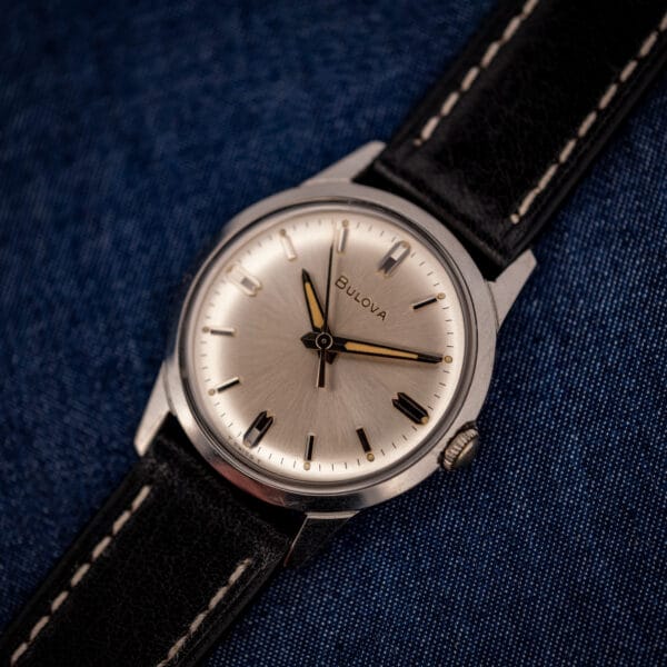 Vintage Bulova manual wind silver sunburst dial flat lay on black leather strap with crown at three