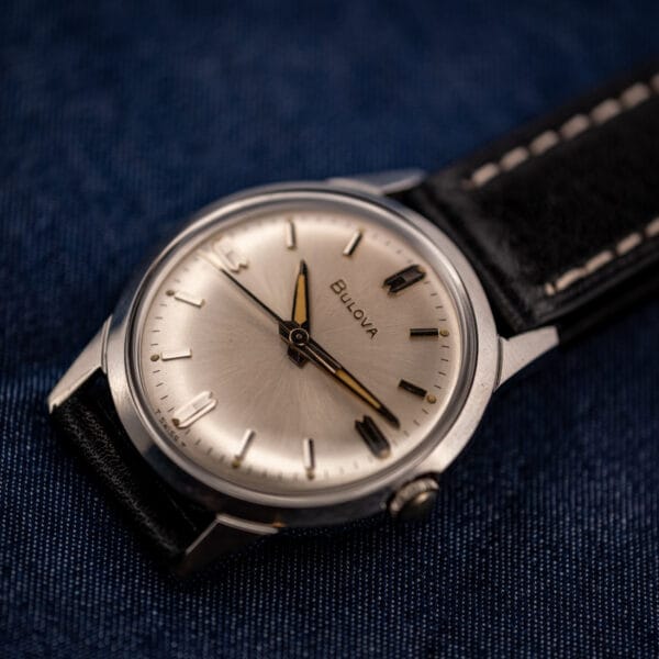 Vintage Bulova manual wind sunburst dial stainless steel watch angled on denim with black leather strap