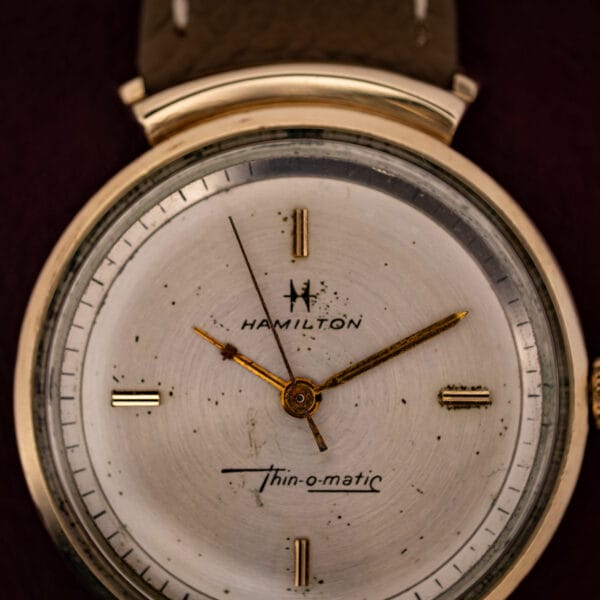 Hamilton Thin-O-Matic dial close-up showing HAMILTON H-logo, applied gold baton markers and dauphine hands with light foxing