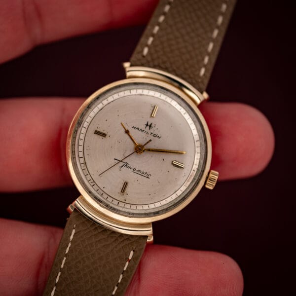 Vintage Hamilton Thin-O-Matic T-406 held in hand showing the dial, integrated hooded lugs and mud grey strap