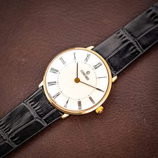 Vintage Concord gold plated watch angled on brown leather, white Roman numeral dial and gold winding crown