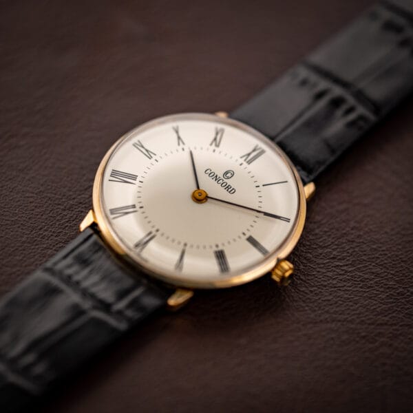 Concord manual wind dress watch angled view, slim gold plated case and cream-toned white Roman numeral dial