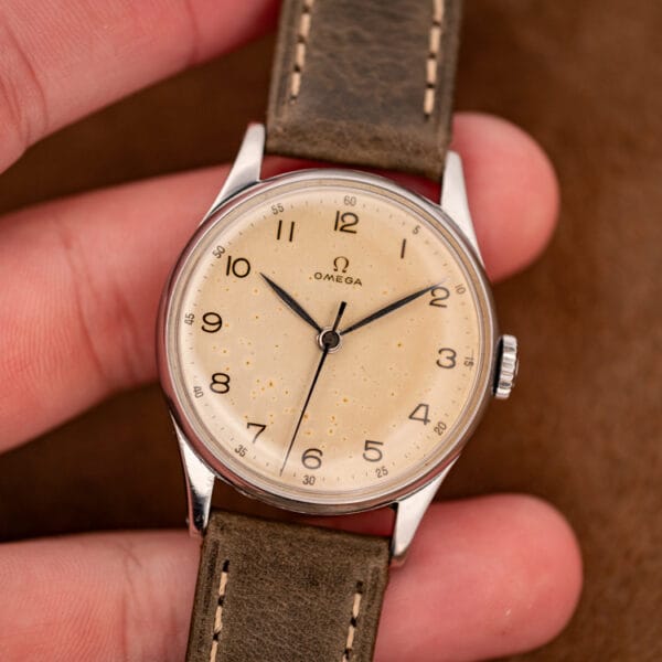 Omega ref. 2391 held in hand, warm eggshell tropical dial with Arabic numerals and blued leaf hands