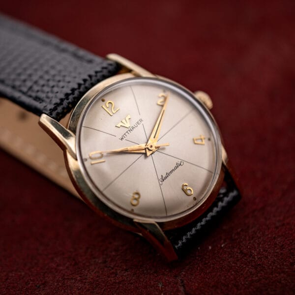 Vintage Wittnauer 2673-11SR automatic, starburst sector dial and gold filled case shown at an angle on burgundy