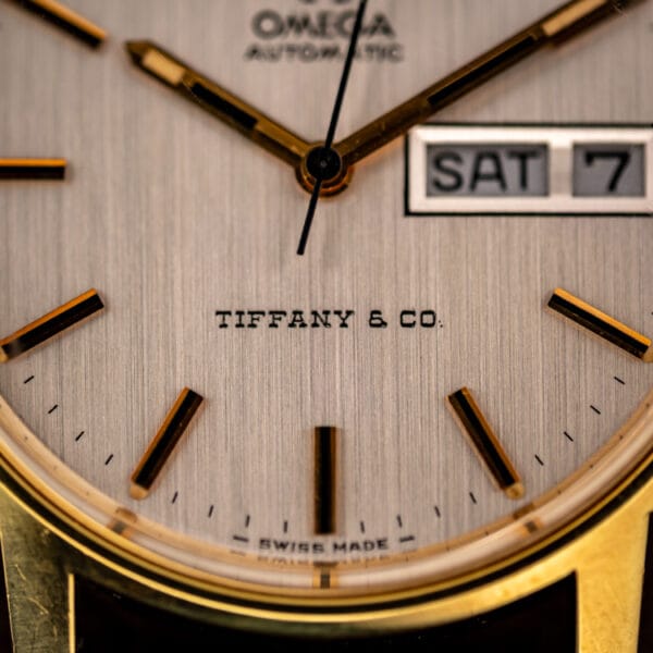 Macro of the Omega dial showing the Tiffany and Co. signature above SWISS MADE with faceted gold baton markers