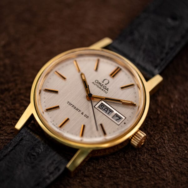 Angled view of the Omega 166.0117 gold-plated case, Omega-signed crown at three and Tiffany and Co. day-date dial