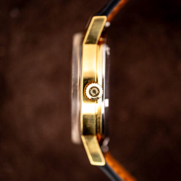 Side profile of the Omega gold-plated case with the Omega-signed crown at the three position