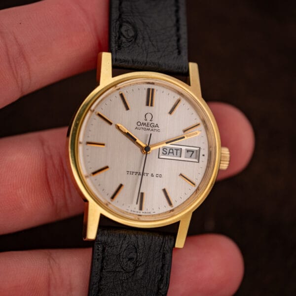 Omega Tiffany and Co. 166.0117 held in hand, silver day-date dial and gold-plated case in daylight