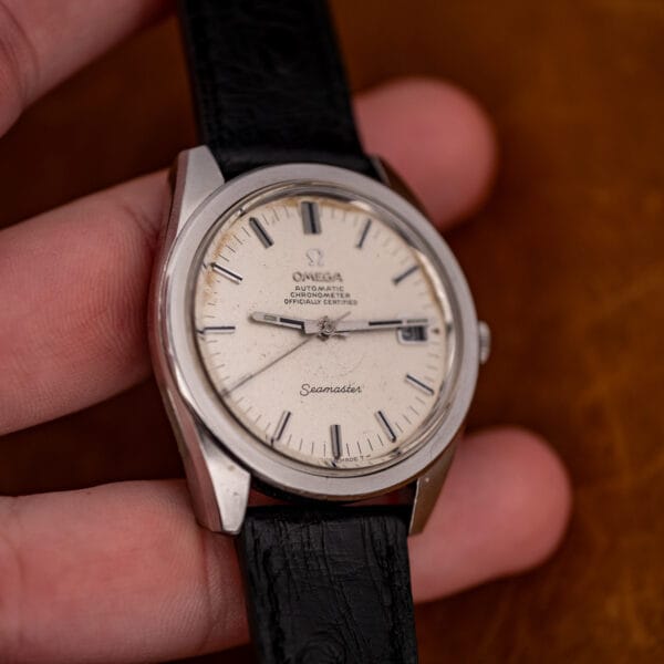 Omega Seamaster 168.022 held in hand, straight-on dial with visible foxing and the black ostrich strap trailing.