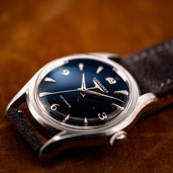 Vintage Longines automatic 6536-1 black dial on grey suede strap, three-quarter profile of the bombe case