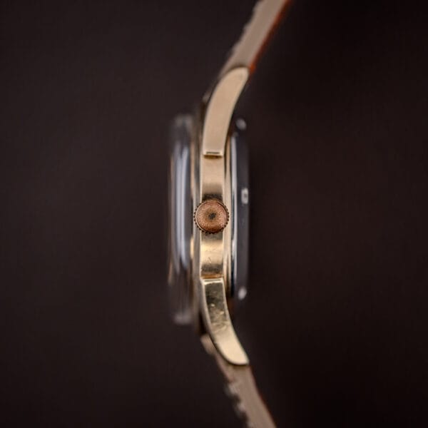 Tissot gold-filled case profile with fluted crown showing honest wear beneath a domed acrylic crystal
