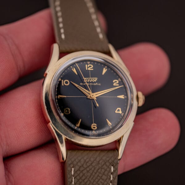 Vintage Tissot bumper automatic held in hand showing the 33.5mm gold-filled case and black gilt dial