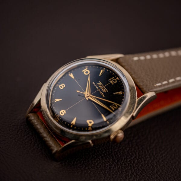 Vintage Tissot 28.5-21 gold-filled case and black gilt dial angled on a dark leather surface