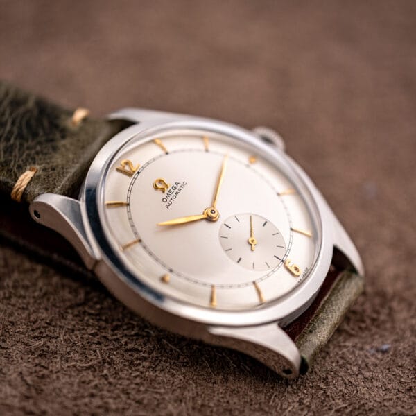 Low-angle Omega 2421/4 showing tapered downturned lugs, olive leather strap and silvered sector dial