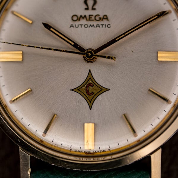 Omega 14765 dial close-up: red-C four-point logo emblem above the T SWISS MADE T tritium line