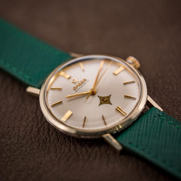 Omega caliber 552 silver dial three-quarter view with slim gold hands and applied red-C logo cartouche