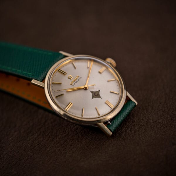 Omega Automatic ref. 14765 three-quarter view, gold bezel case on pine green Saffiano strap with tan underside