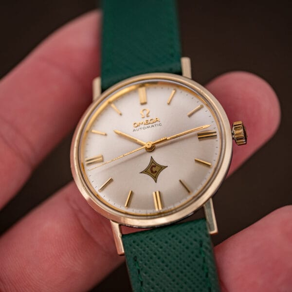 Omega Automatic caliber 552 in hand, silver sunburst dial, 14k gold bezel, pine green Saffiano leather strap