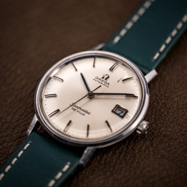 Omega Seamaster De Ville 166.020 on a green leather strap, framed date window showing the numeral seven.