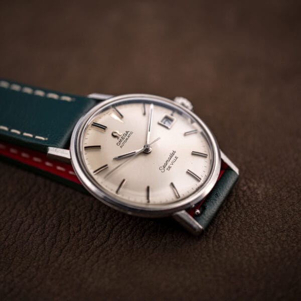Stainless steel Omega Seamaster De Ville 166.020 on green leather, showing slim faceted hands with light age patina.