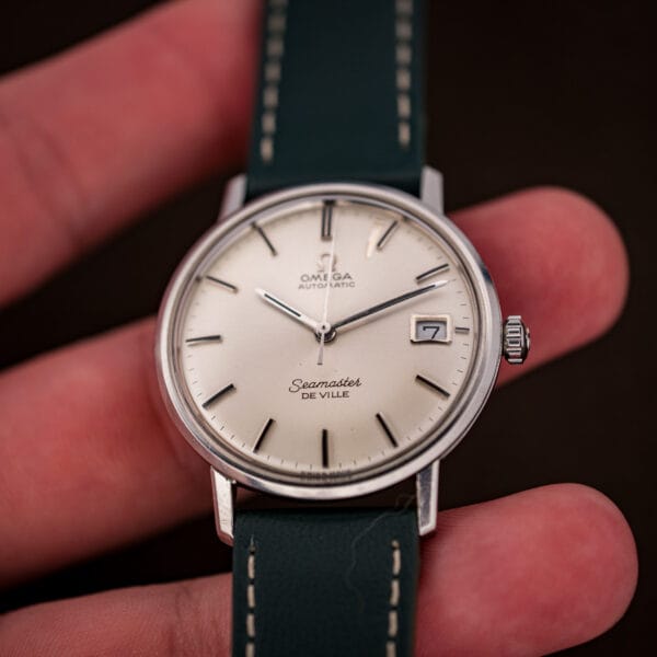 Omega Seamaster De Ville 166.020 held in hand, silver dial and date window showing seven under natural light.