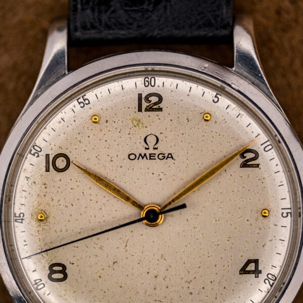 Aged cream Omega dial with applied gold dot markers, gilt Arabic numerals and even foxing beneath the Omega symbol at twelve
