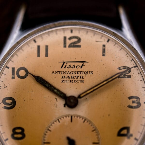 Macro of the Tissot Antimagnetique dial showing the Barth Zurich co-signature and tropical salmon patina beneath painted Arabic numerals.