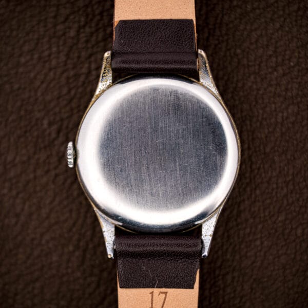 Brushed stainless snap caseback of the vintage Tissot, honest brassing at the lug tips above a 17mm leather strap.