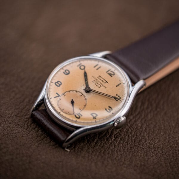 Angled studio shot of the Tissot Antimagnetique Barth Zurich dial, salmon tone deepening toward the center.