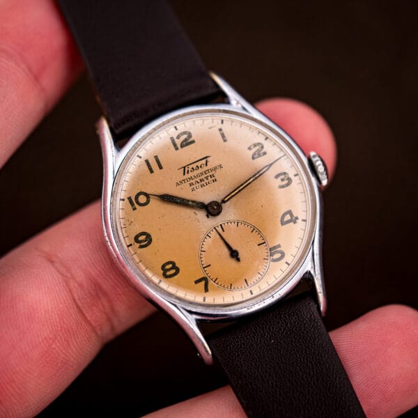 Vintage Tissot Antimagnetique held in hand, showing the compact 33.5mm case and salmon Barth Zurich dial.