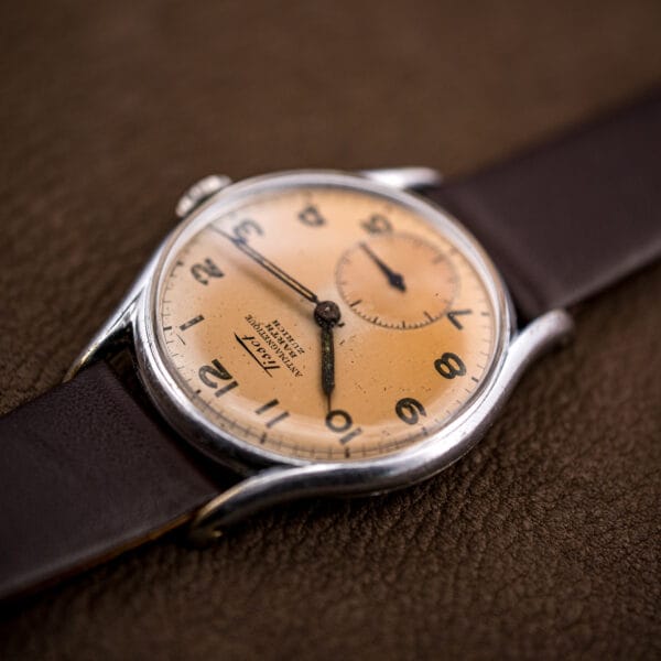 Tissot Antimagnetique ref. 6439-2 on brown leather, warm salmon dial glowing against a dark background.